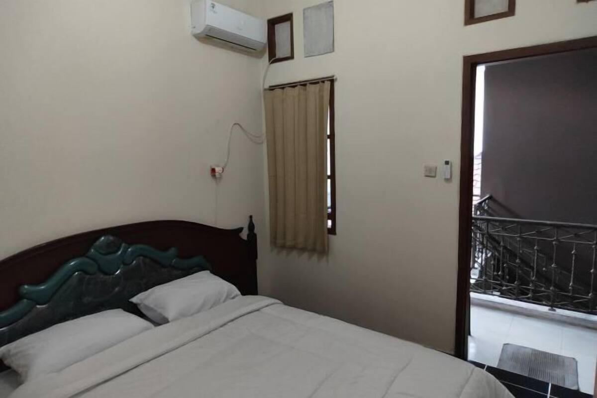 A bedroom with a bed, an air conditioner, a window with curtains, and a door leading to a balcony.