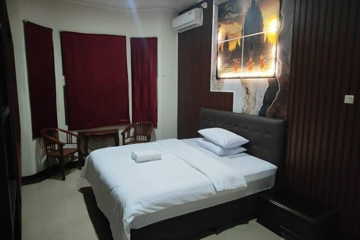 A hotel room with a bed, a desk, two chairs, and a wall-mounted air conditioner.