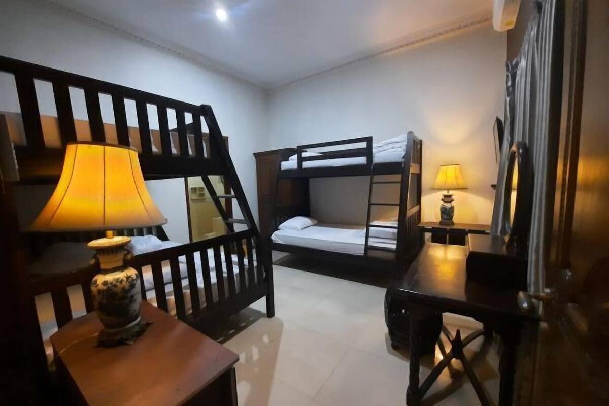 A room with bunk beds, a wooden chair, a small table with a lamp, and a desk with a lamp.