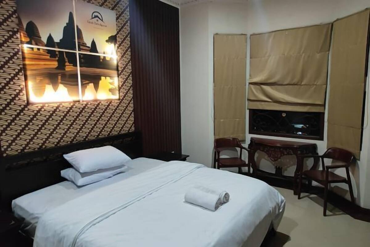 A hotel room with a bed, two chairs, a desk, a TV, and a patterned wall.