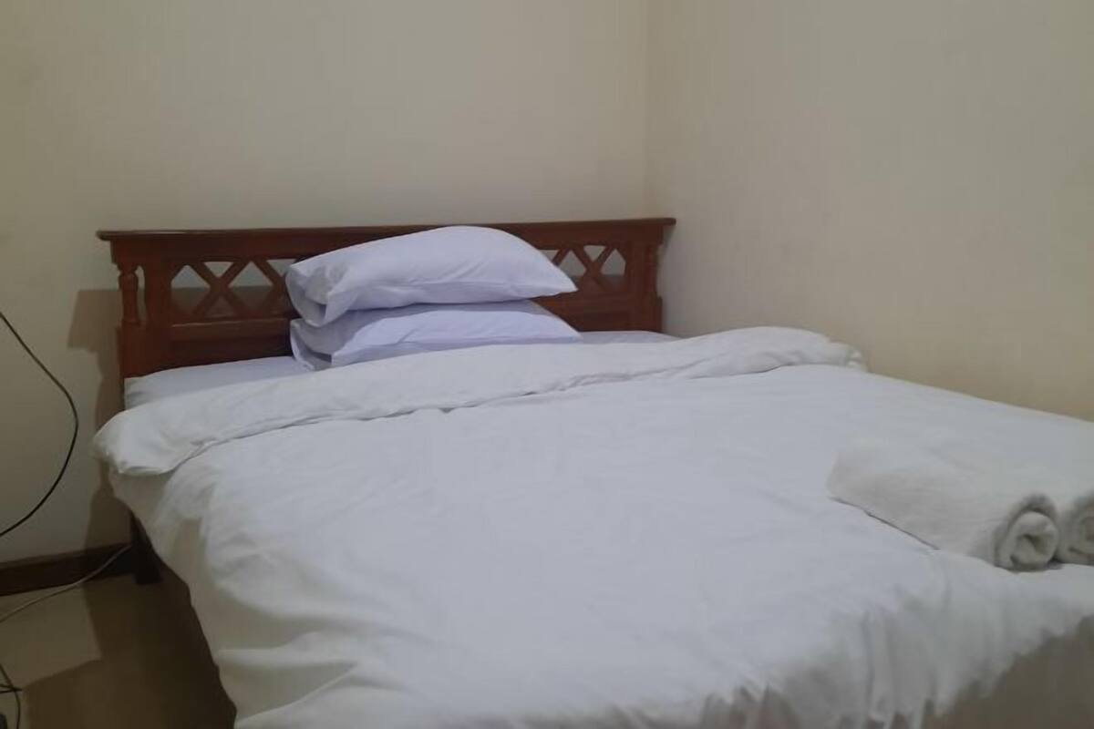A neatly made bed with white linens and a wooden headboard.