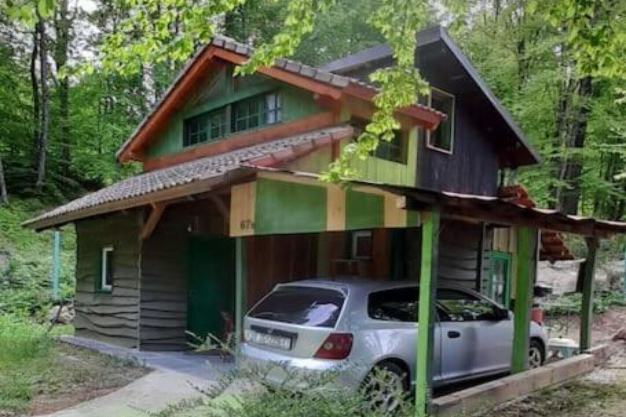A rustic cabin with a car parked in front, surrounded by dense forest.