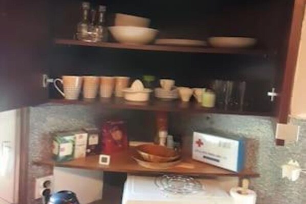Een keuken met planken vol kommen, bekers en een doos cornflakes.