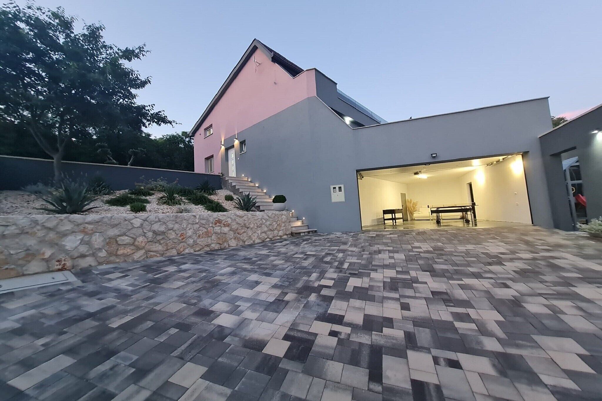 A modern house with a paved patio, a stone wall, and a garage.