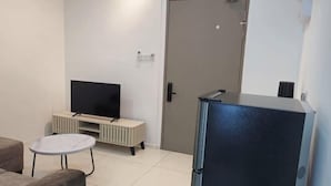 A living room with a flat-screen TV, a small round table, a sofa, and a refrigerator. - BaySuites by Alawa Homes (Kota Kinabalu)