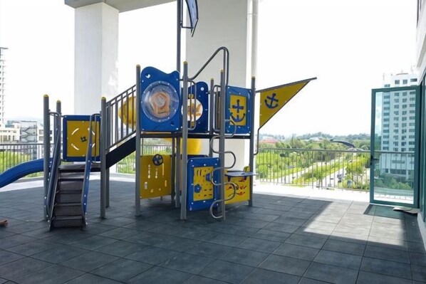 A playground with a blue and yellow play structure, a staircase, and a glass elevator. - BaySuites by Alawa Homes (Kota Kinabalu)