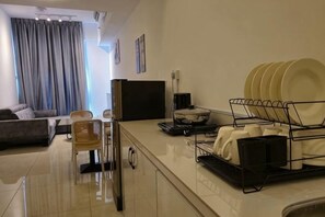 A modern living room with a sofa, a dining table, and a kitchen area with a dish rack. - BaySuites by Alawa Homes (Kota Kinabalu)