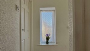 Ein schmaler Flur mit Holzdielen, einer weißen Tür und einem Fenster mit weißem Vorhang.