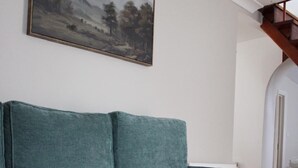 Ein Wohnzimmer mit einem türkisfarbenen Sofa, einem dunkelbraunen Hocker und einem Bild an der Wand.