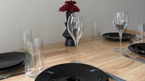Ein Esstisch ist gedeckt mit schwarzen Tellern, klaren Gläsern und einer Vase mit roten Blumen.
