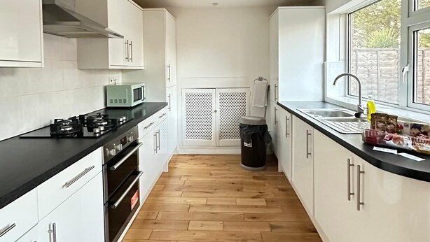 Eine moderne Küche mit weißen Schränken, einer schwarzen Arbeitsplatte und Holzboden.