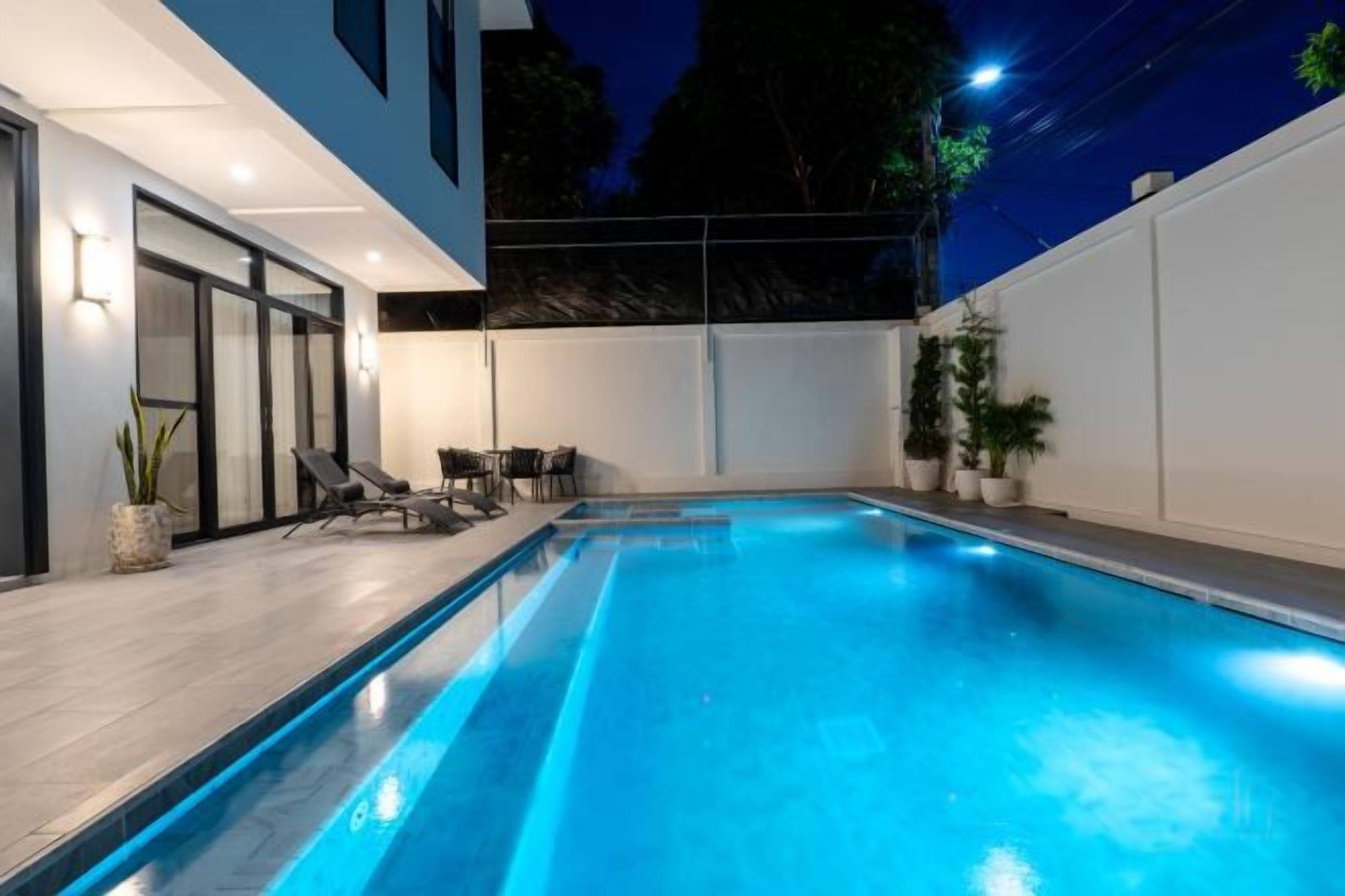 Piscina com design moderno, rodeada por um espaço de estar com mobiliário e plantas em vasos.
