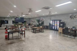 Une pièce spacieuse équipée de plusieurs tables et chaises, d’un téléviseur et de distributeurs automatiques.