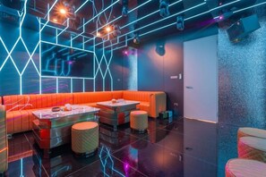 A modern lounge area with a neon-lit geometric ceiling, a red cushioned seating area, and a polished floor. - T M L-Urban 4 Bedroom-Independent Swimming Pool and Ktv (Pattaya)