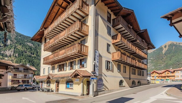 A multi-story hotel with wooden balconies, a sign for 'Blauer', and a view of mountains in the background. - Beautiful apartment for 6 people with WIFI and TV (Pinzolo)