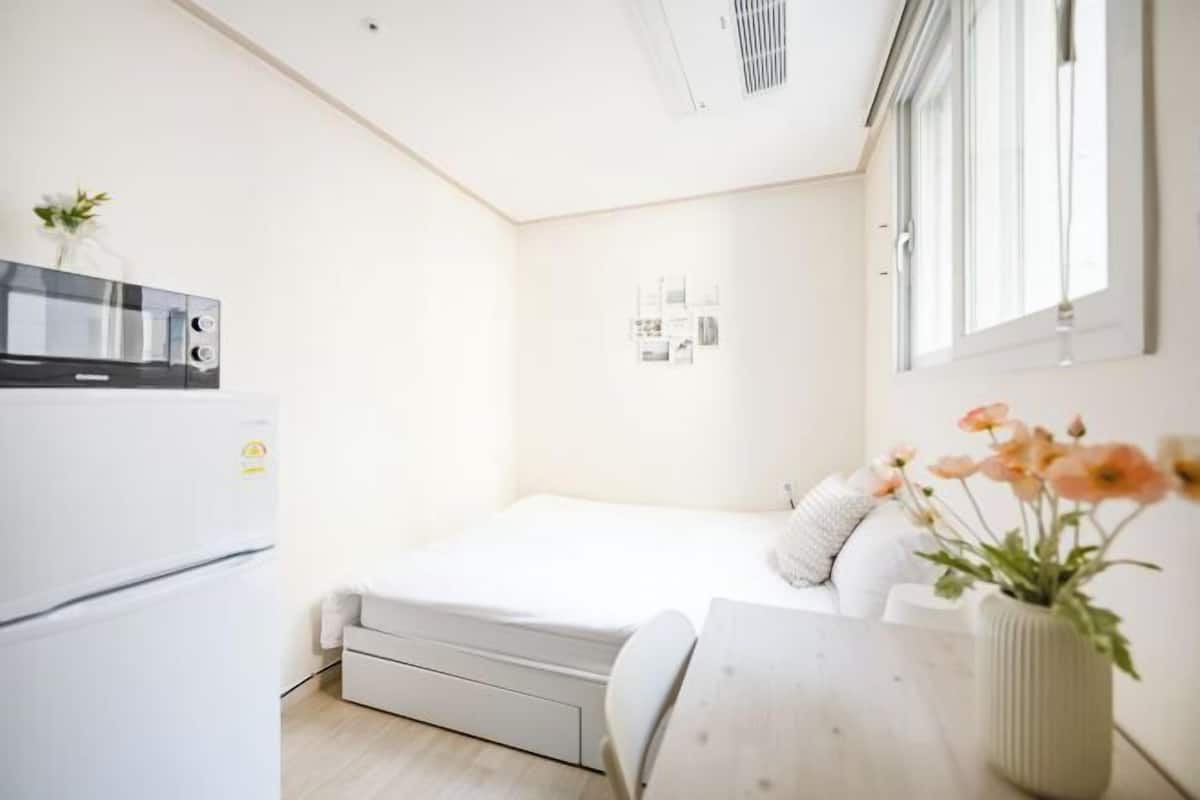 A compact room with a bed, a small table, a refrigerator, and a window with a view.