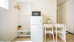 A compact room with a white refrigerator, a small table with chairs, a hanging clothes rack, and a potted plant. - Ehwa Blossom (Seoul)