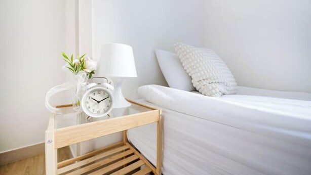 A neatly arranged bedroom with a wooden bedside table holding a white alarm clock and a small vase with flowers. - Ehwa Blossom (Seoul)
