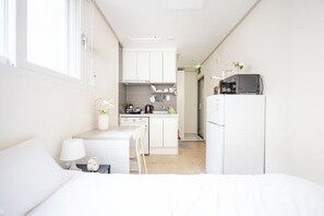 A compact hotel room with a bed, bedside table, lamp, and a kitchenette area including a microwave and a refrigerator. - Ehwa Blossom (Seoul)