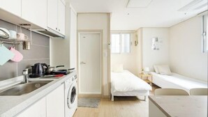 A compact hotel room with a kitchenette, a single bed, a small desk, and a window. - Ehwa Blossom (Seoul)