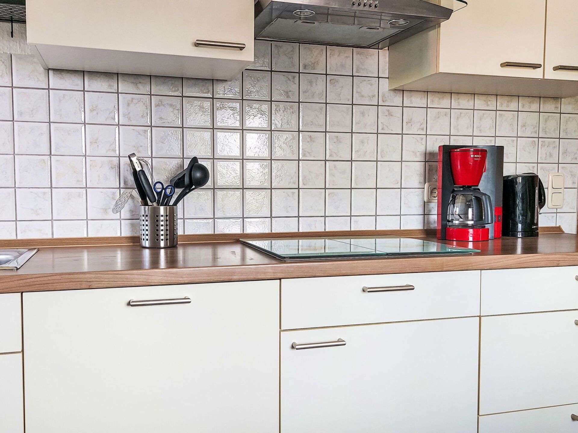 Una cocina con armarios blancos, salpicadero de mármol y una cafetera sobre la encimera.