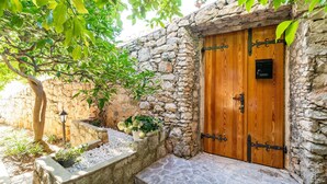 A stone wall with a wooden door, a tree, and a small garden area with plants and a lamp post. - Villa Vista Old Town - Four Bedroom House with Terrace and Sea View (Cavtat)