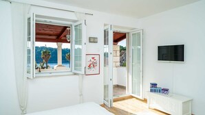 A bedroom with a large window, a bed, a TV, and a balcony with a view of the sea. - Villa Vista Old Town - Four Bedroom House with Terrace and Sea View (Cavtat)