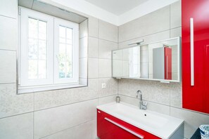 A modern bathroom with a white sink, red cabinet, and a large mirror.