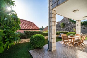 A patio with a stone table and chairs, surrounded by greenery and a stone wall.