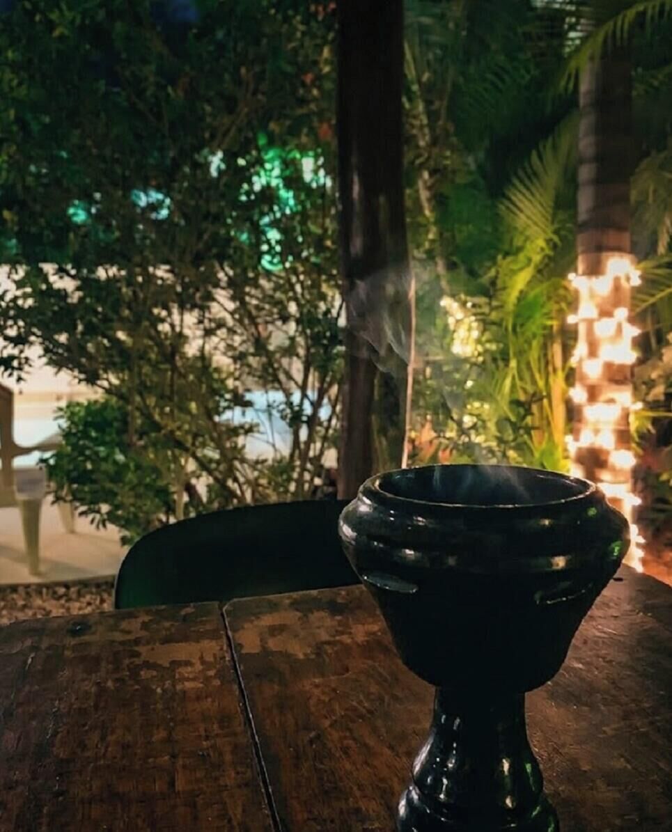 A black ceramic cup on a wooden table outdoors with greenery and string lights in the background.