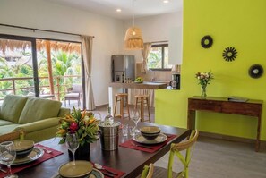 A dining area with a table set for four, a kitchen in the background, and a view of the outdoors.