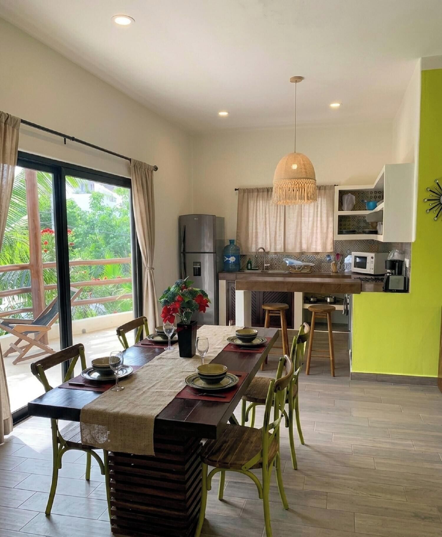 A modern kitchen with a dining area, large windows, and a view of greenery.