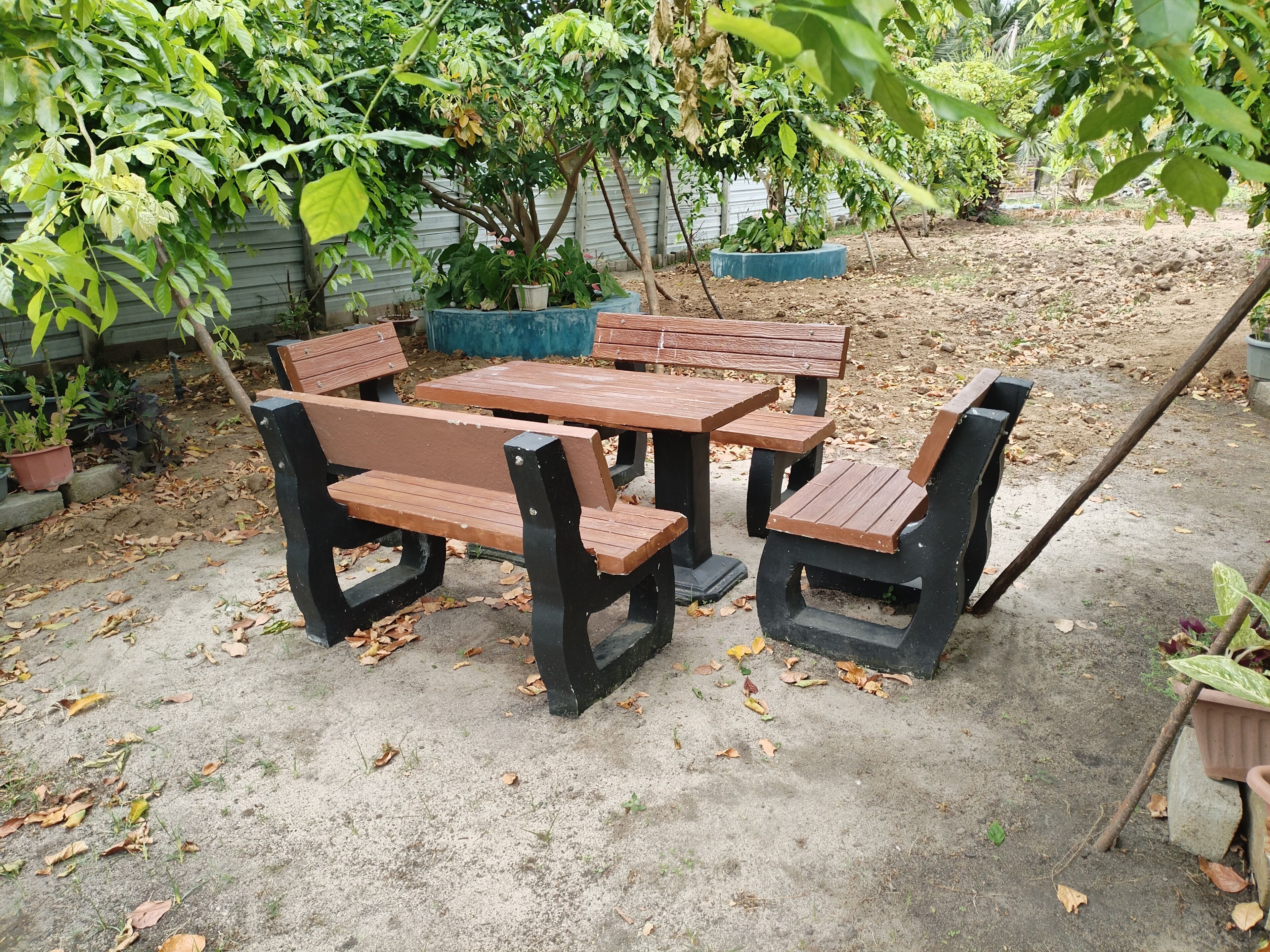Een tuinpatio met een houten tafel en banken, omringd door potplanten en bomen.