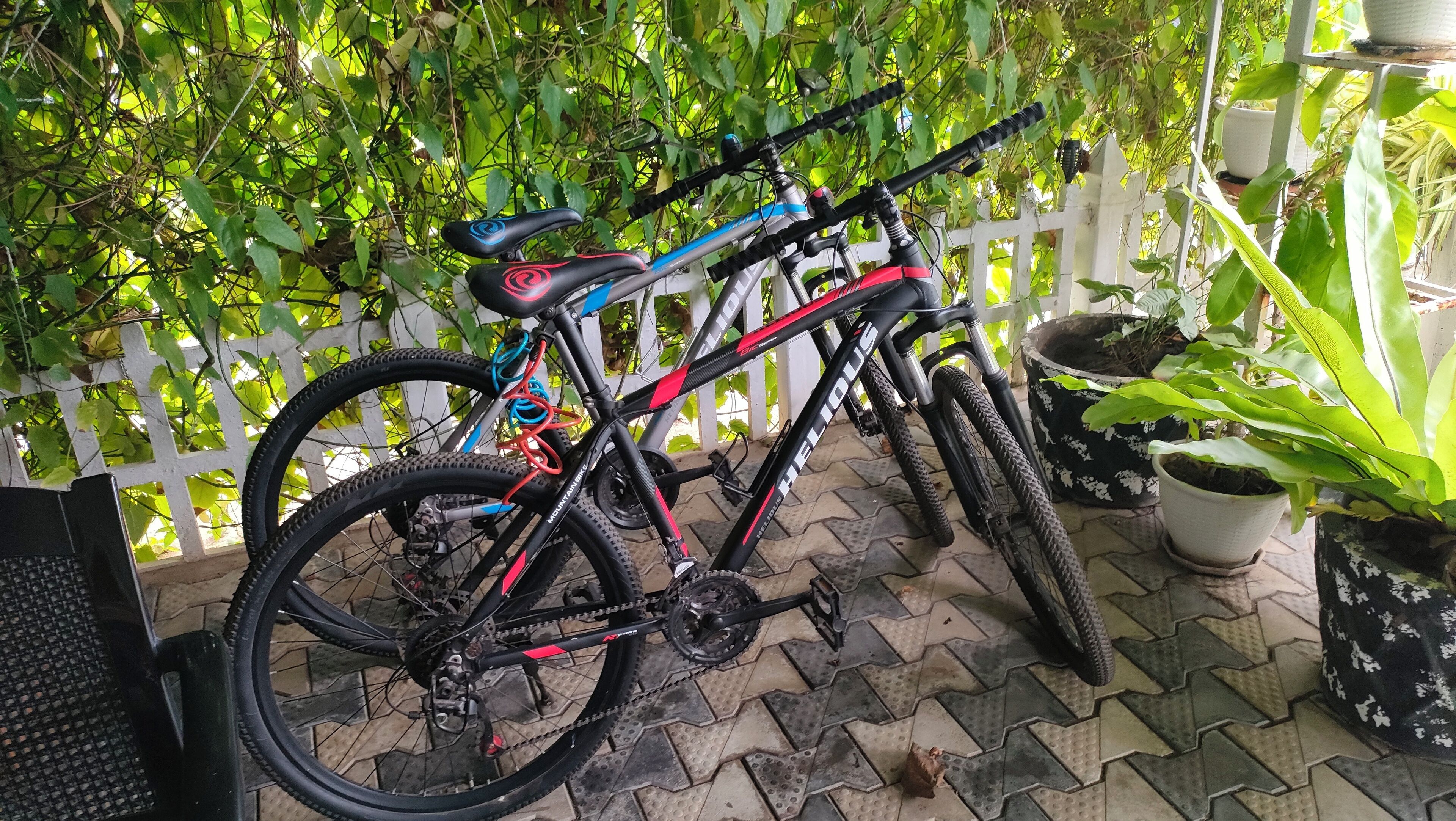 A bicycle parked on a tiled patio with a white fence and potted plants in the background.