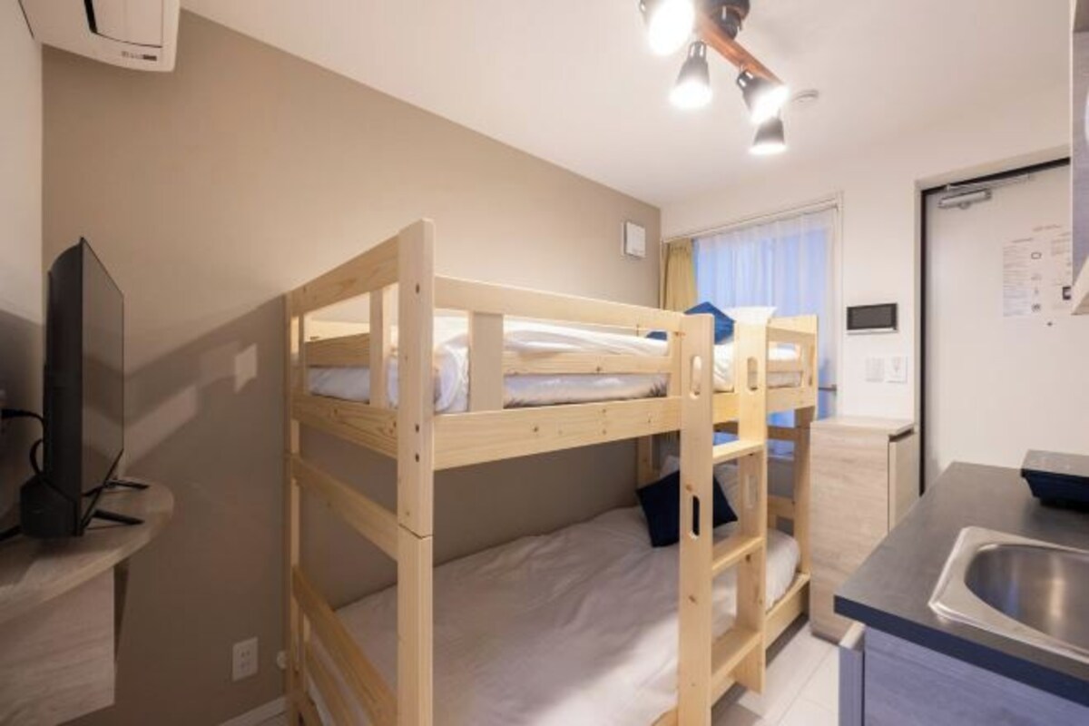 Ein Stockbett, ein Schreibtisch mit Computer, ein Waschbecken und ein Fenster mit Vorhängen.