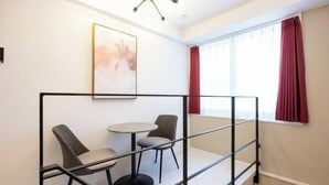 A room with a balcony, a small round table, two chairs, a framed picture on the wall, and a window with red curtains. - Retaw Hills Waseda (Tokyo)