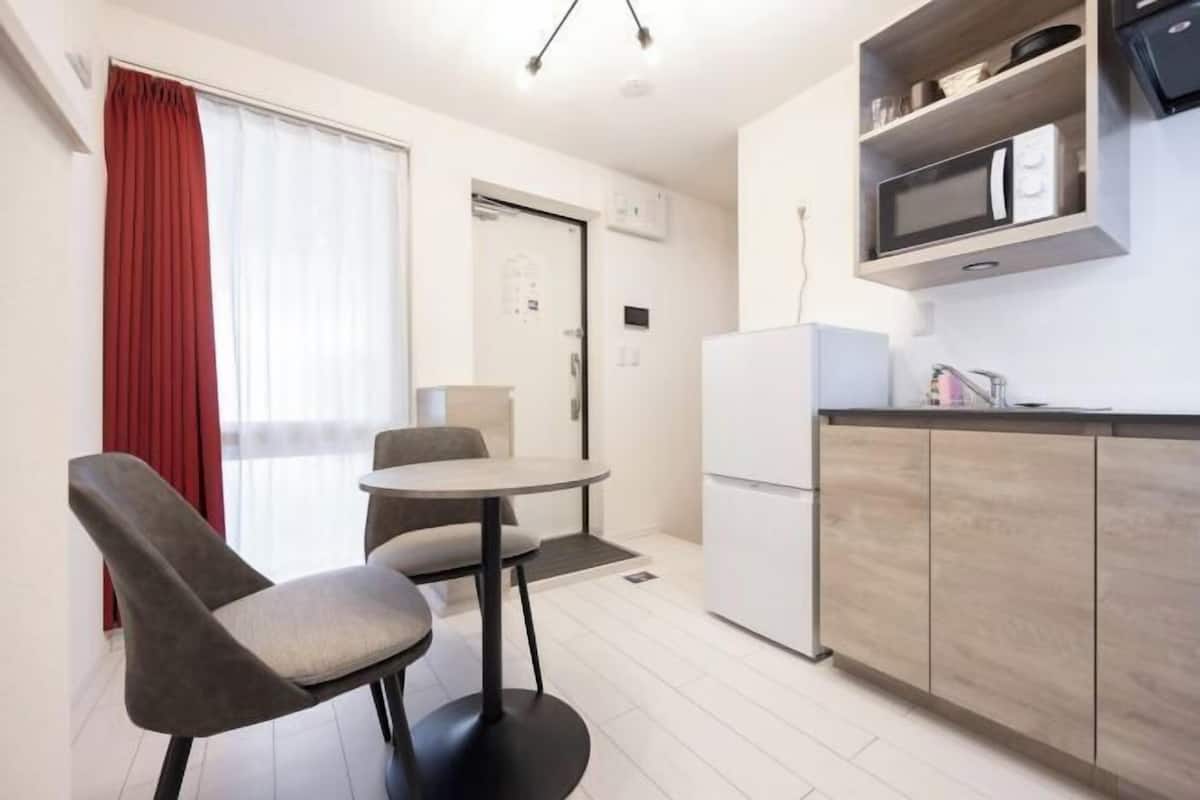 A compact kitchen with a refrigerator, microwave, and wooden cabinets. There is a small dining area with two chairs and a table.