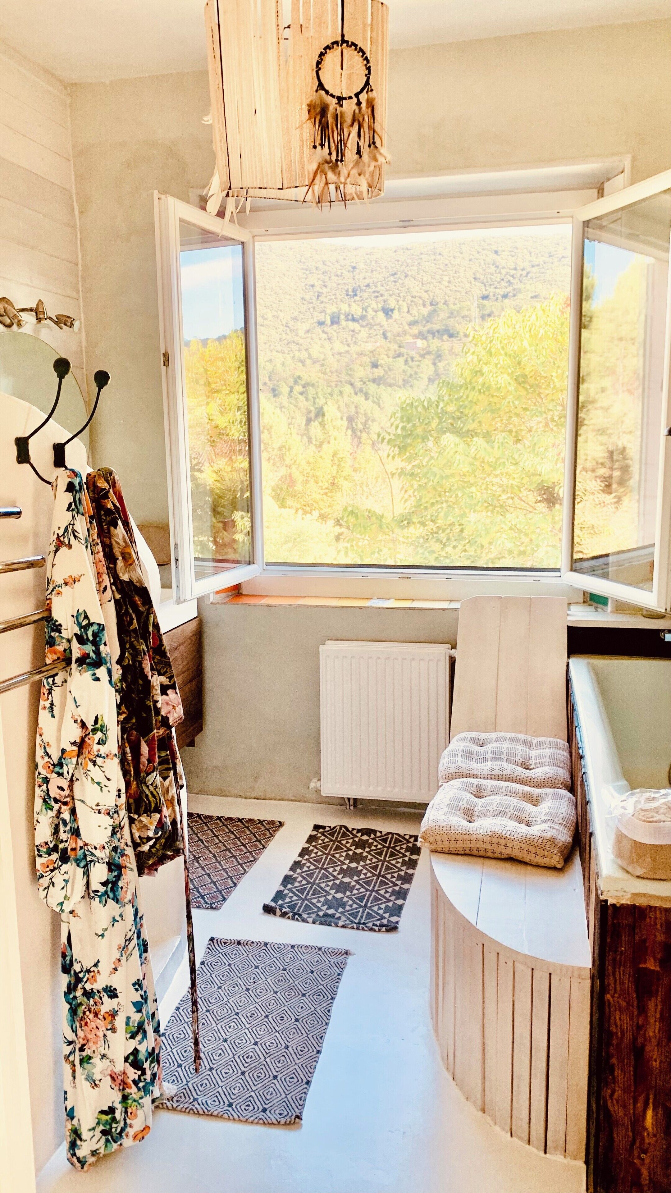A room with a large window, a radiator, a wooden bench, and a dreamcatcher.