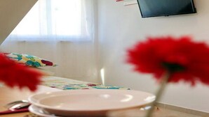 Zona pranzo con tavolo apparecchiato per due, televisione a parete e finestra con tende.