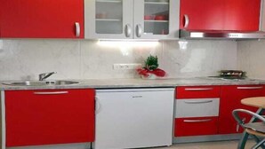 Una cucina con mobili rossi, una lavastoviglie bianca e un lavello in acciaio inossidabile.