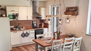 A modern kitchen with white cabinets, a wooden countertop, and a dining area with a wooden table and white chairs. - Beautiful apartment for 5 people with WIFI, TV and balcony (Sattendorf)