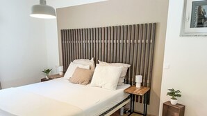 A modern bedroom with a wooden slat headboard, a bed with white linens, a bedside table with a lamp, and a small plant. - Beautiful apartment for 5 people with WIFI, TV and balcony (Sattendorf)