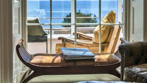 A room with a view of the ocean through large windows. There are two chairs, one with a cushion and a book on it, and another with a cushion. - Beautiful  villa for 10 people with WIFI, terrace and pets allowed (Cawsand)