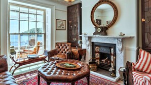A traditional room with a fireplace, leather furniture, and a large window overlooking a scenic view. - Beautiful  villa for 10 people with WIFI, terrace and pets allowed (Cawsand)