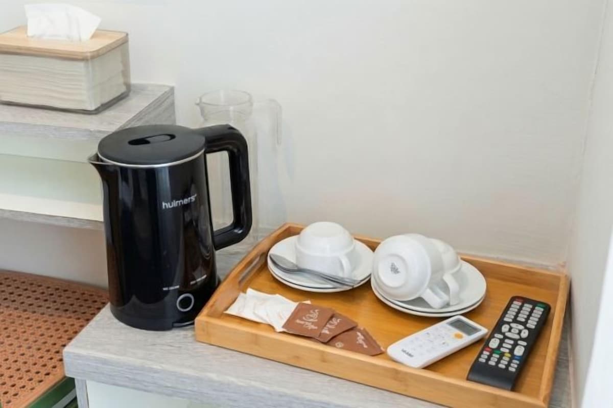A tray with a coffee maker, cups, saucers, a remote control, and a chocolate bar on a hotel counter.