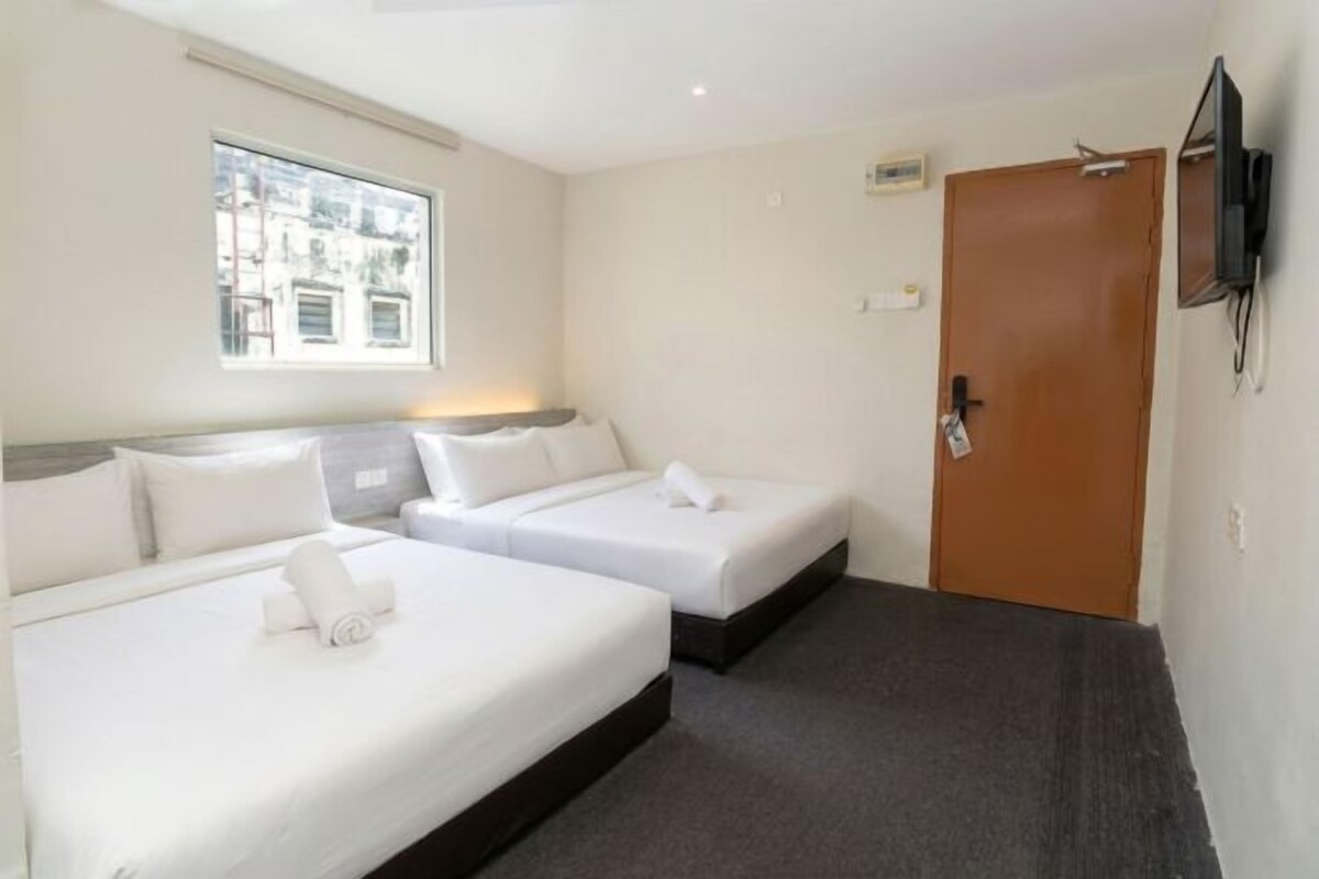 A hotel room with two beds, a television mounted on the wall, and a window providing natural light.