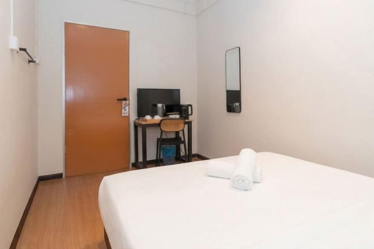 A hotel room with a bed, a desk with a chair, a television, and a door.