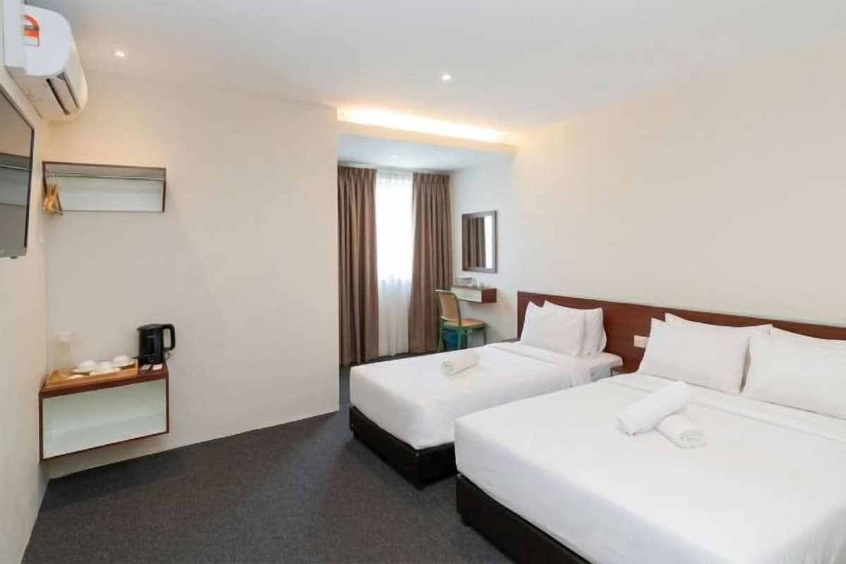 A hotel room with two beds, a desk with a chair, a mirror, and a window with curtains.