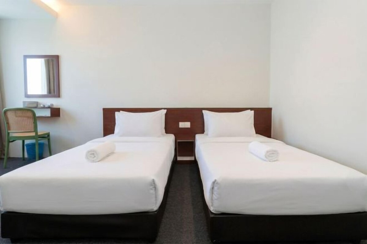 A hotel room with two single beds, a chair, and a small table.