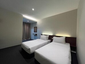 Una habitación de hotel con dos camas individuales, una mesita de noche, una lámpara de pared y una puerta que da a un baño.